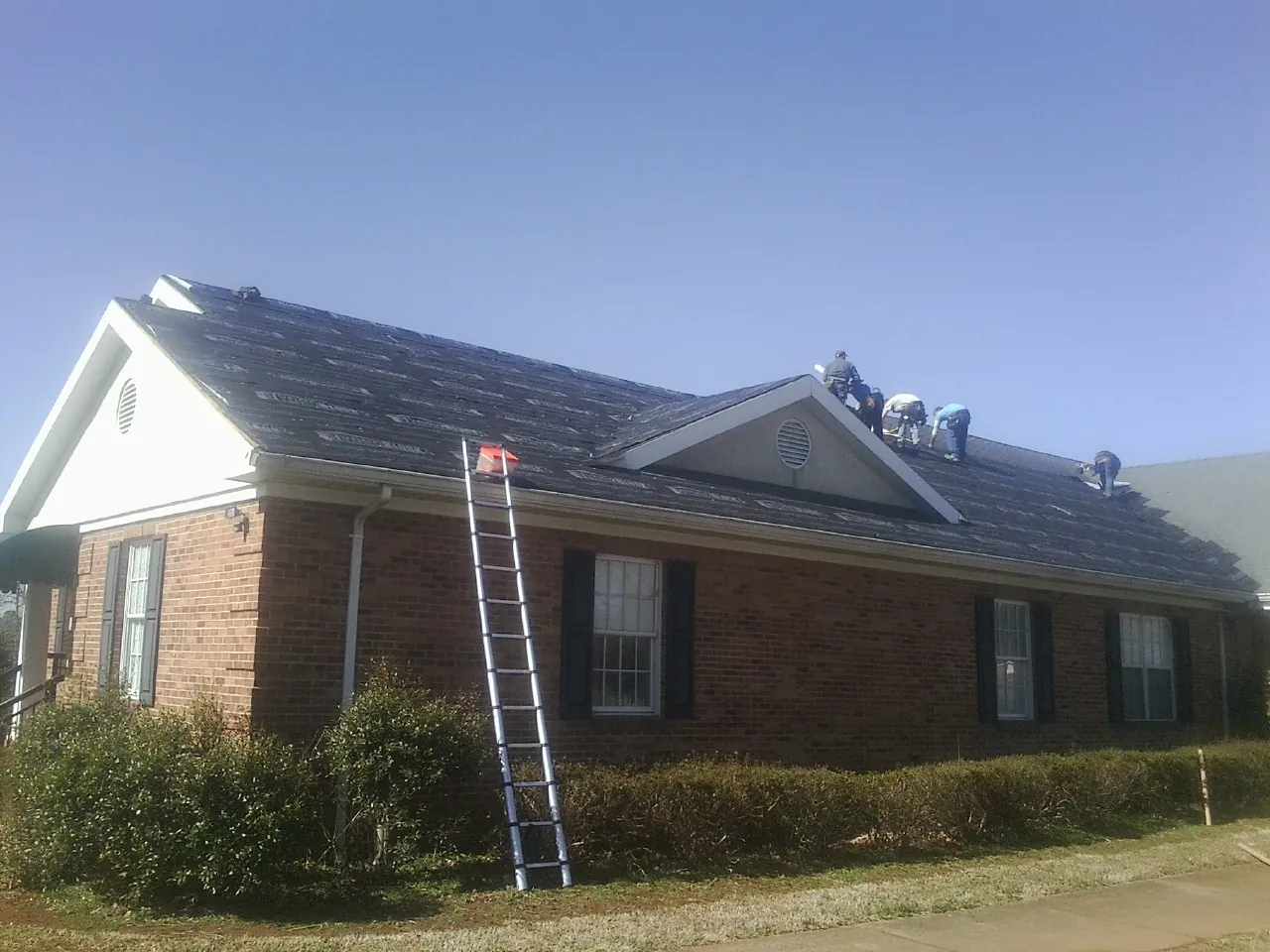 Crew tearing shingles off a brick ranch roof with a ladder set — Metal Roof Repair work by our crew in Crab Orchard