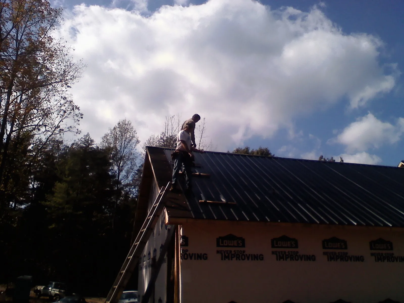 Roofer fastening dark metal panels high against a cloudy sky, from a Roof Inspection job in Crab Orchard